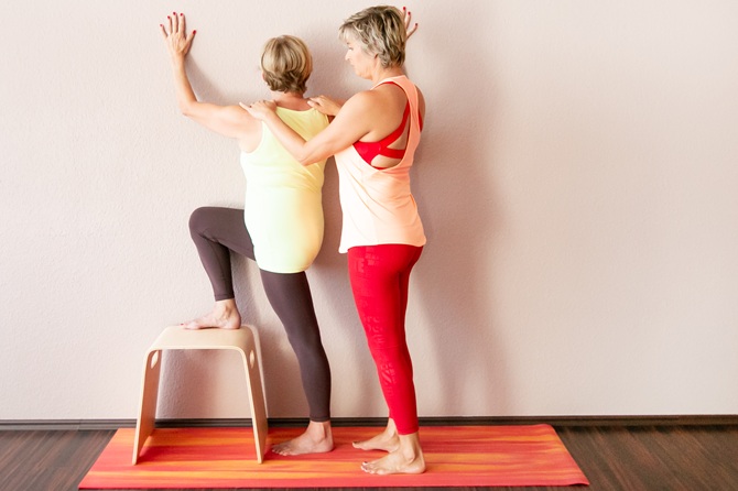 1fach Yoga | 1fach Gesund - Kurs Yoga 50+ - Silke Wagner bei Übung mit Schülerin im Stand an der Wand