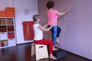 1fach Yoga | 1fach Gesund - Team - Silke Wagner bei therapeutischer Einzelstunde mit Patientin bei Übung an der Wand