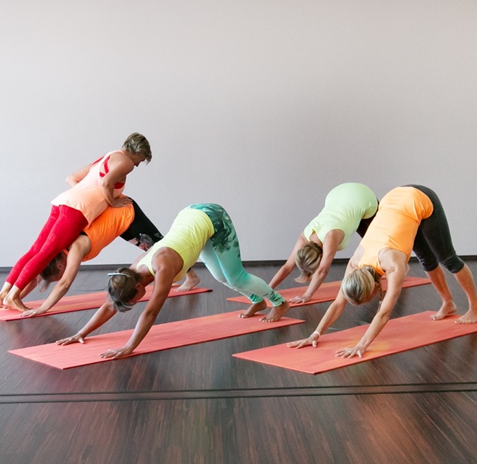 1fach Yoga | 1fach Gesund - Kurs Power Yoga - Silke Wagner korrigiert eine Schülerin im Kurs im herabschauenden Hund